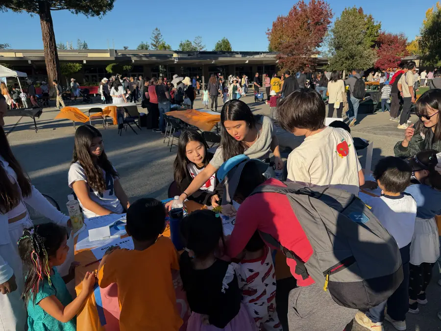 A tight scrum of small children crowds a club table where teen volunteers lean in to help.