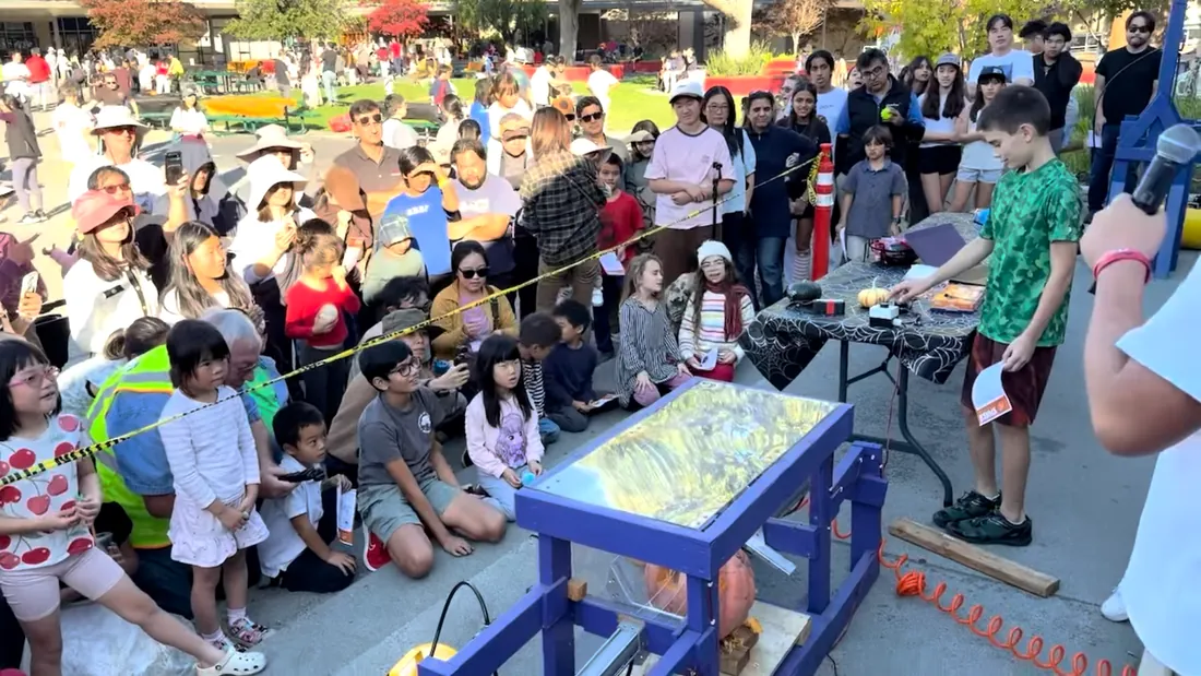 A boy reaches for the smasher’s control button while dozens of children sit and stand along the caution tape watching.