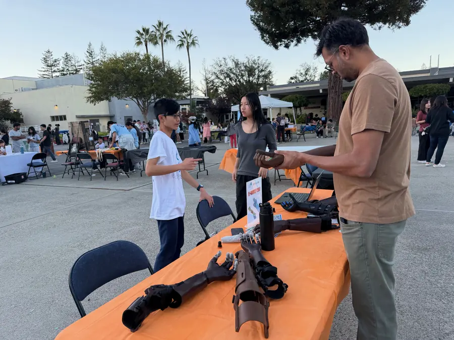 A student explains a 3D-printed prosthetic hand to a visitor turning one over in their hands.