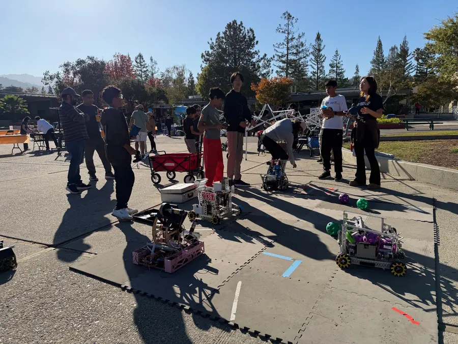 An FTC demo field laid out on foam tiles in the courtyard with three competition robots and scattered game balls.