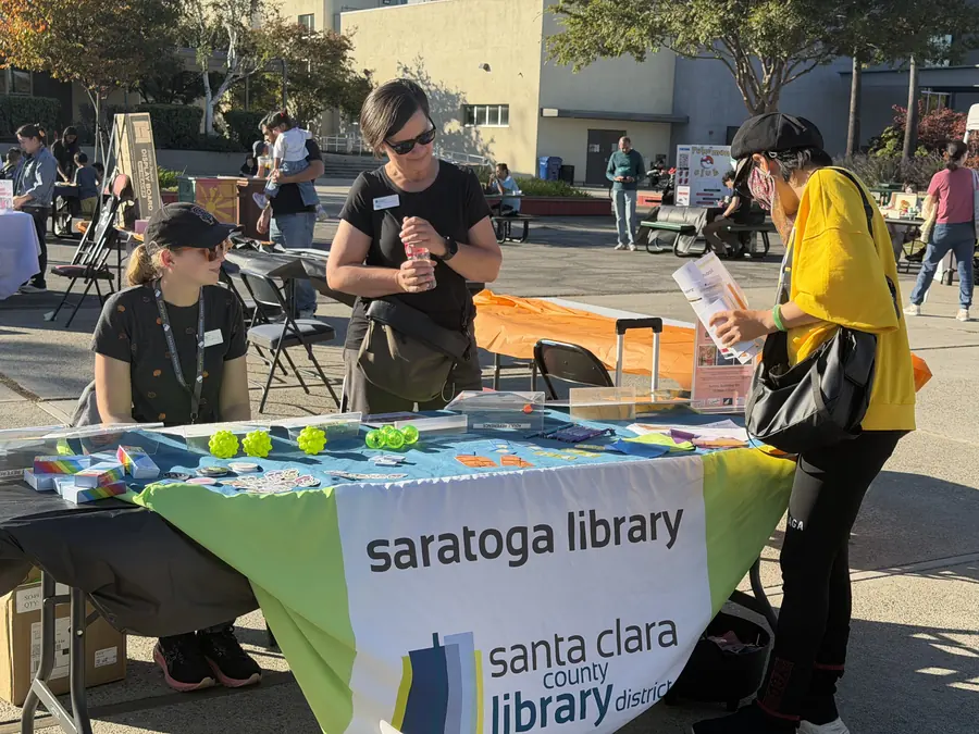 Two Saratoga Library staffers chat with a visitor flipping through material at their community booth.