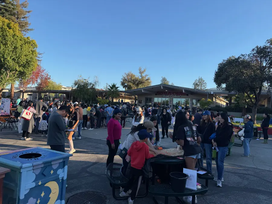 The full Saratoga courtyard packed with hundreds of visitors under a deep blue sky, booths and tables ringing the crowd with the school building at center.