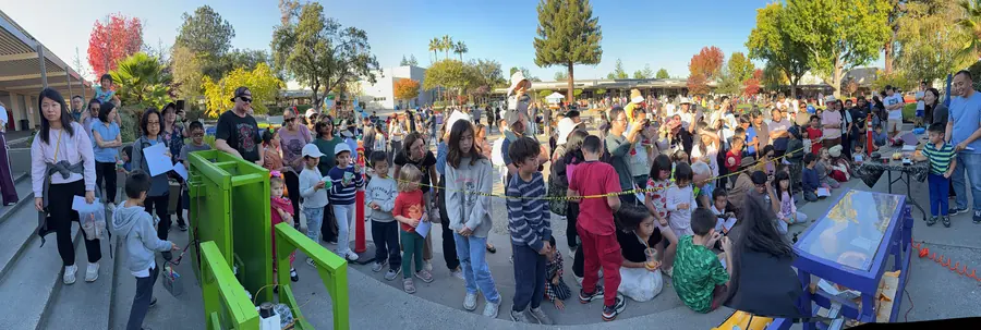 Ultra-wide panorama of the smash zone with the green machine at one end and the blue at the other, a dense arc of families between them.