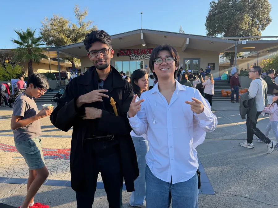 Two grinning high schoolers throw finger-guns for the camera in front of the Saratoga High School entrance at golden hour.